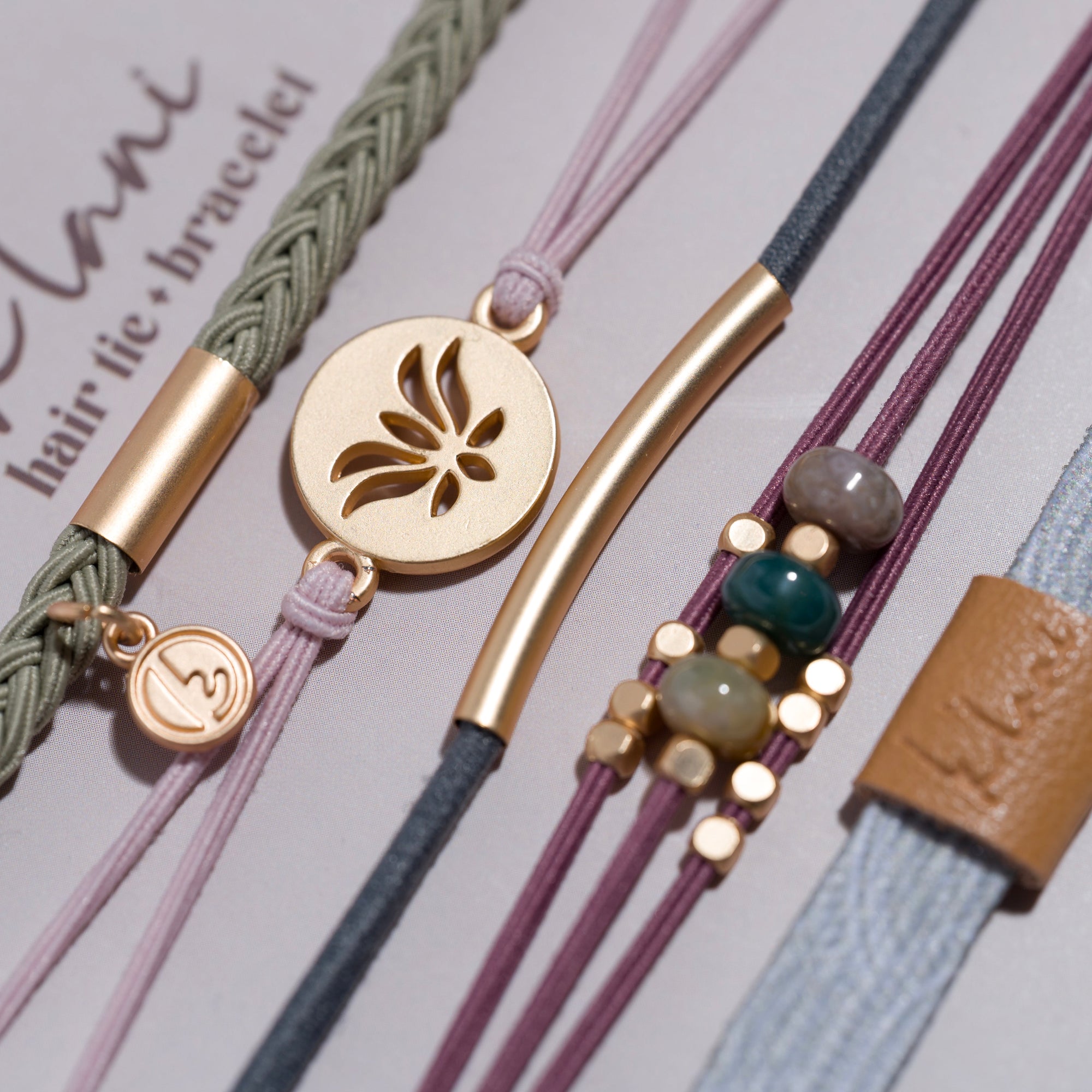 Collection of five hair tie bracelets with gold accents, beads, and varied cord textures on display card