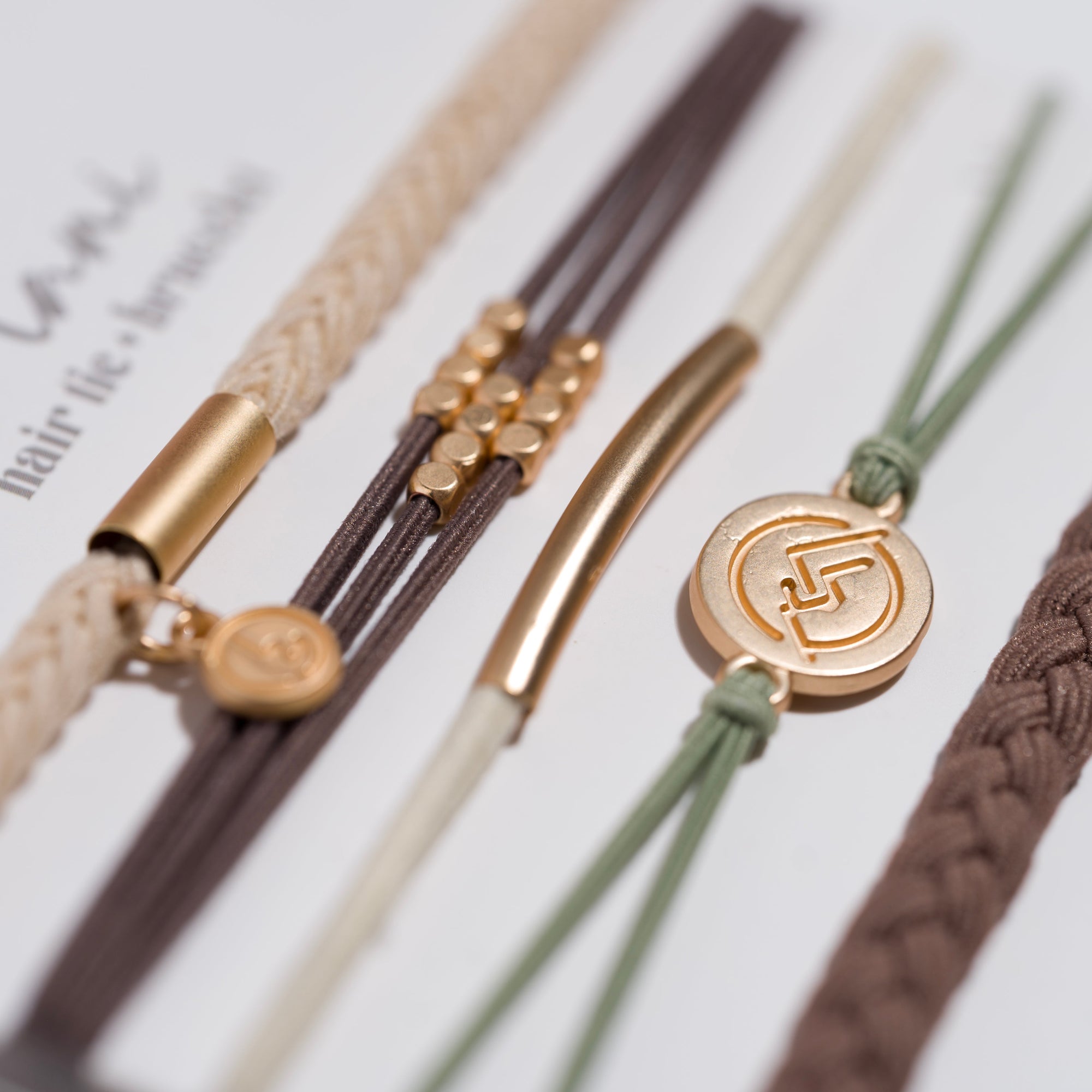 Close-up of five hair tie bracelets in neutral earth tones with gold metal charms and accents