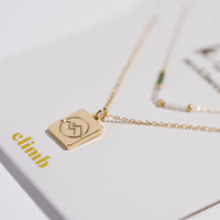 Gold square pendant necklace with mountain motif and layered chain with green beads
