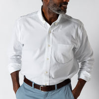 White long-sleeve oxford shirt with button-down collar and chest pocket, worn with light blue pants