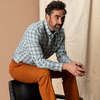 Men's long-sleeve plaid button-down sport shirt in blue and white tartan, worn on model seated on chair