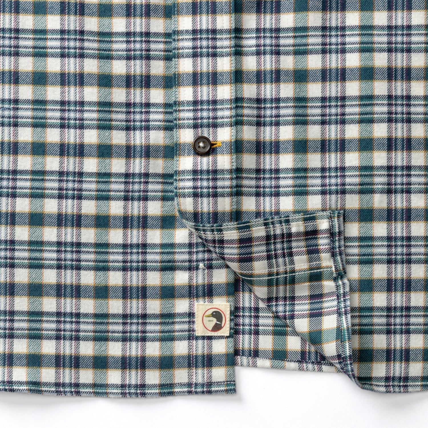 Close-up detail of plaid flannel shirt showing button placket, chest pocket, and brand logo tag