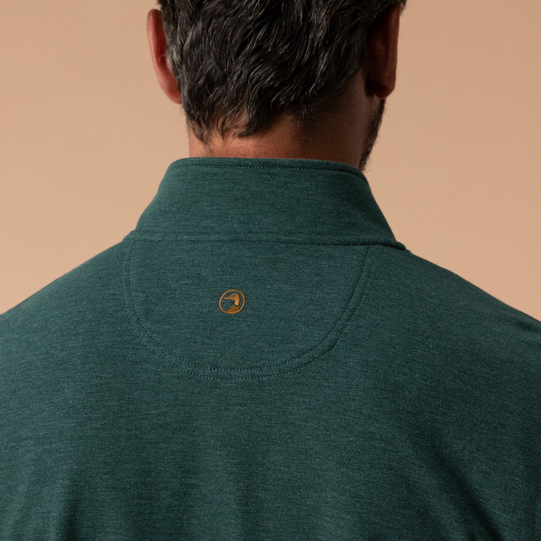 Back view of men's quarter-zip pullover showing collar, loop detail, and circular logo patch