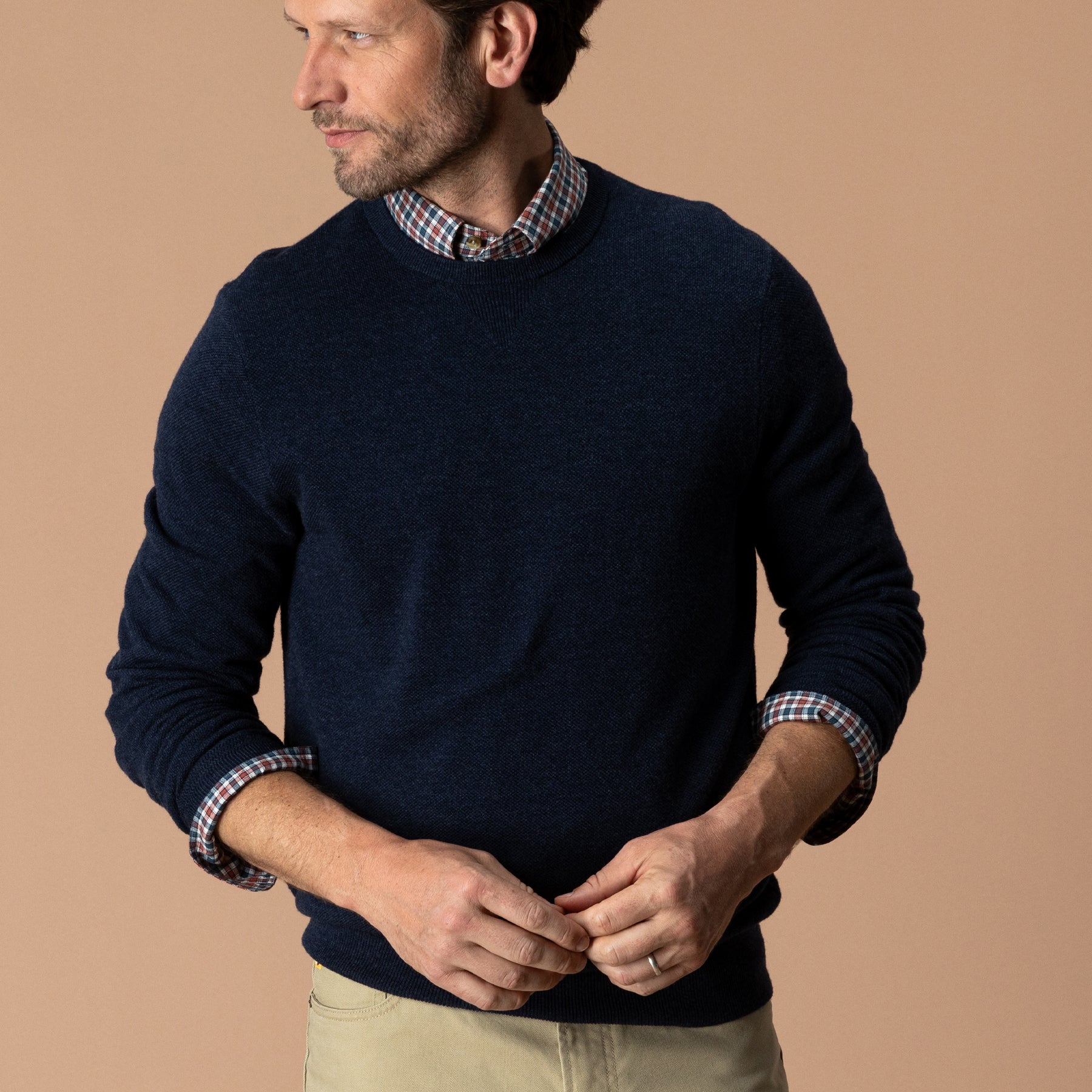 Men's navy crewneck sweater layered over plaid shirt, front three-quarter view