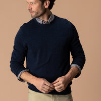 Men's navy crewneck sweater layered over plaid shirt, front three-quarter view