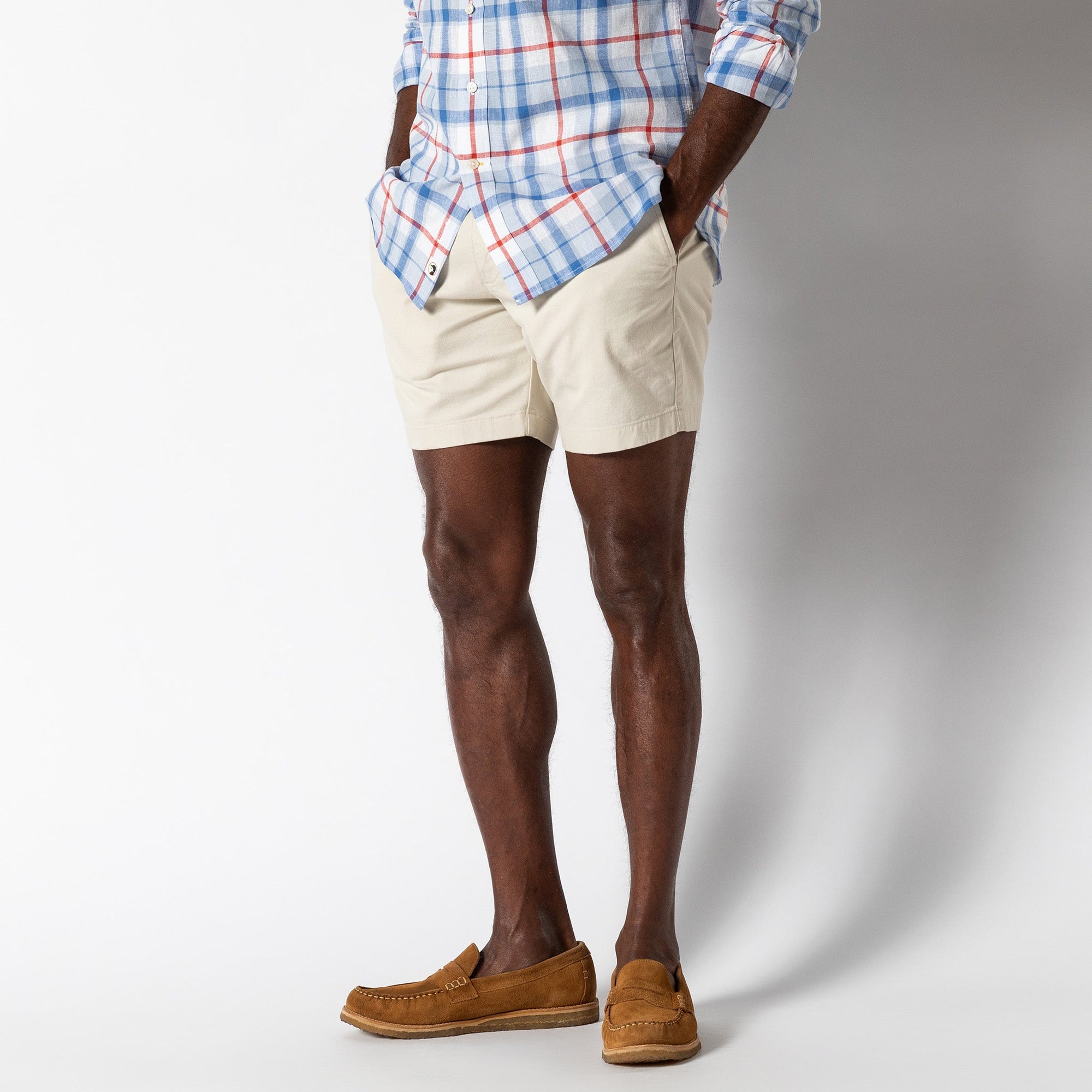 Light beige chino shorts worn with plaid shirt and brown loafers, studio shot