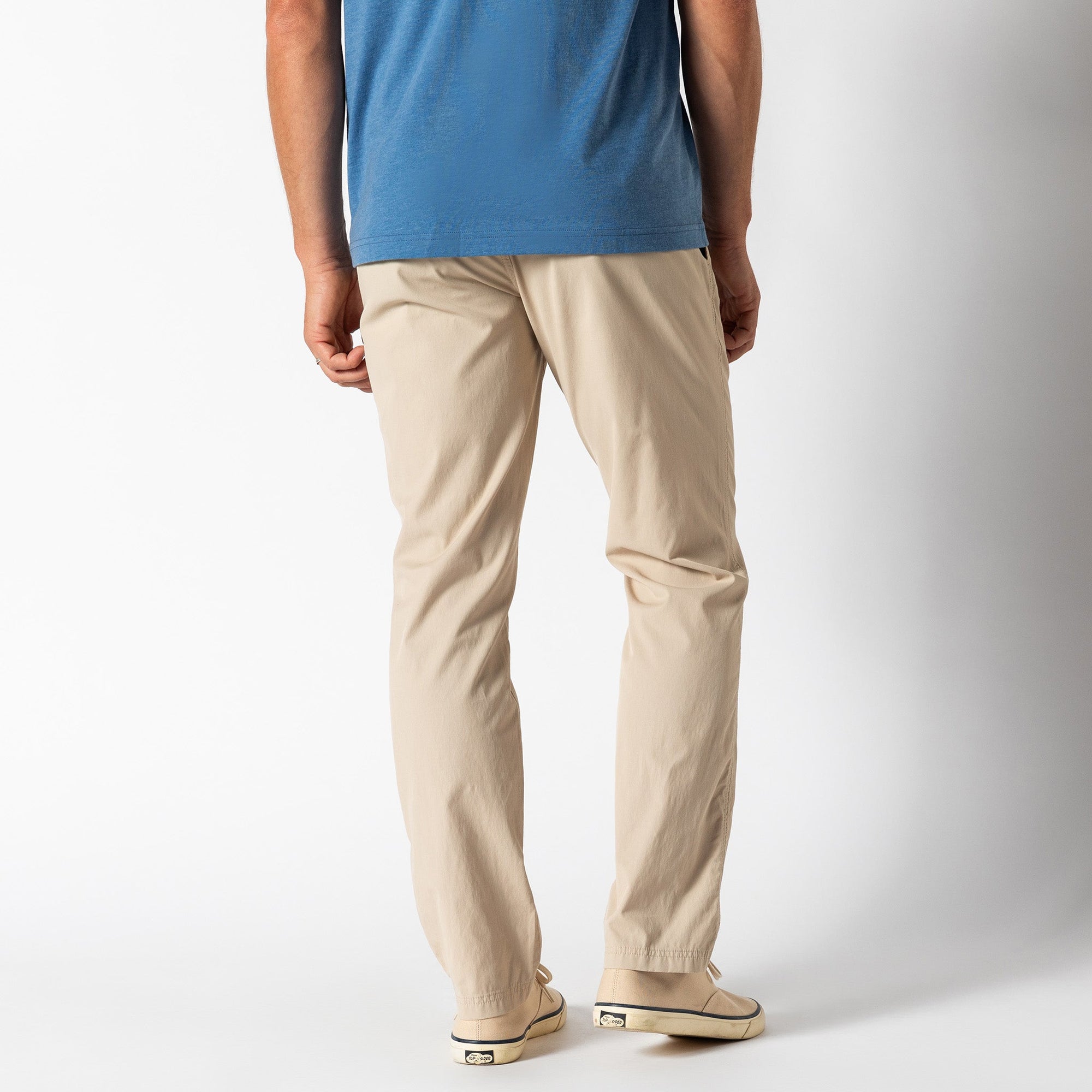 Light beige chino pants worn with blue shirt, back three-quarter view showing fit and silhouette
