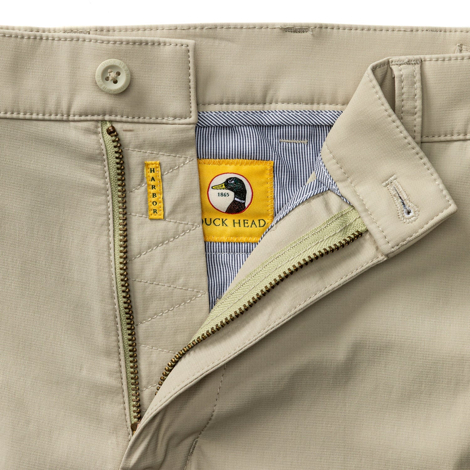 Light tan chino pants with open fly showing striped interior lining and branded waistband detail