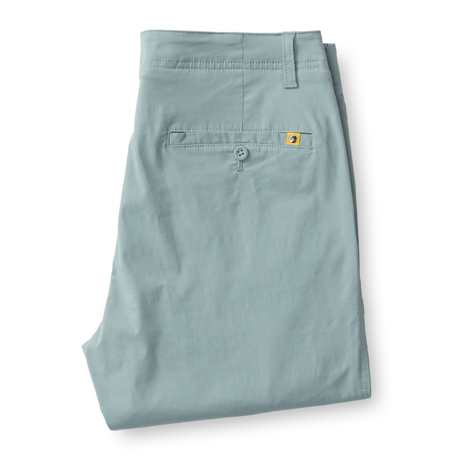 Light green chino pants folded flat showing back pocket with button closure and small logo tab