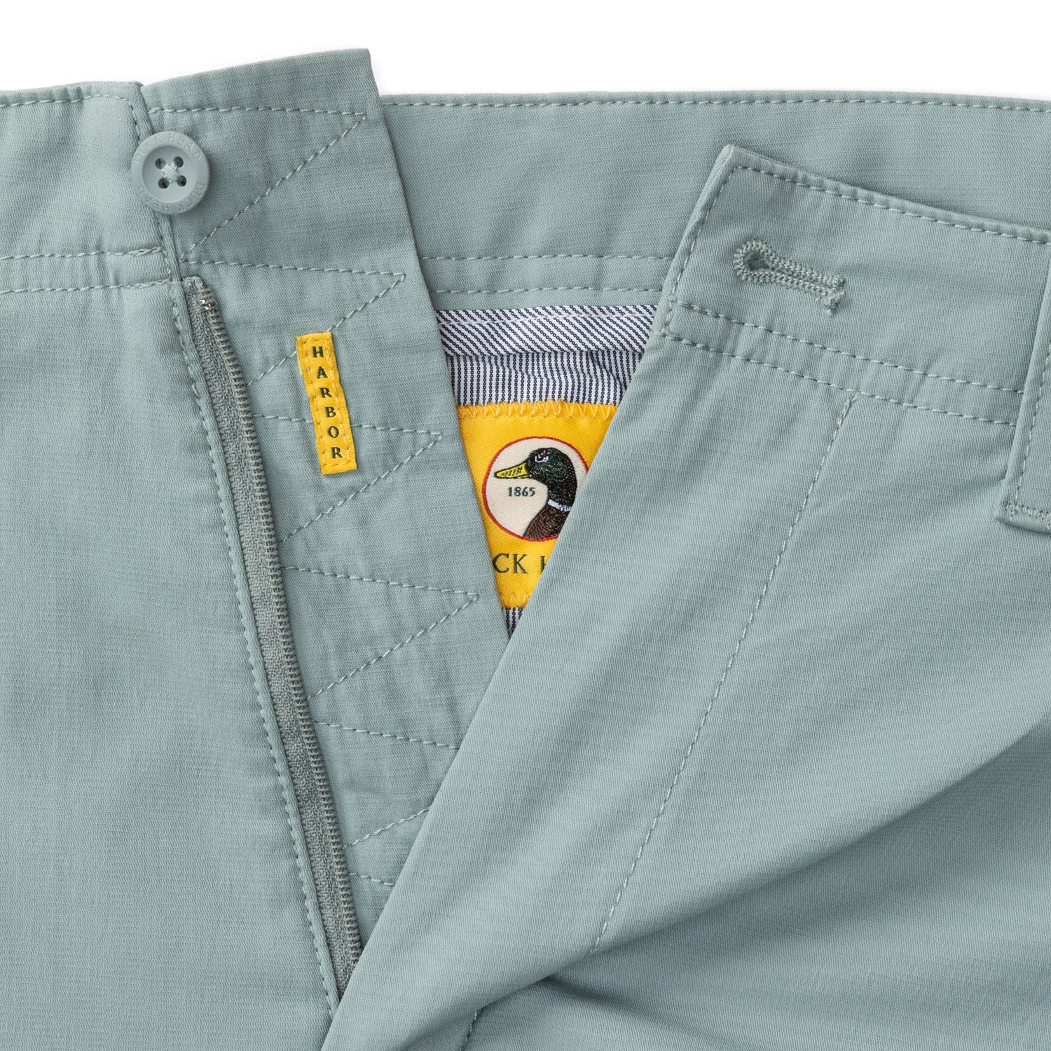 Light colored chino pants detail showing waistband, zipper, and pockets with duck logo