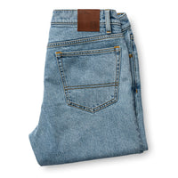 Folded light blue denim jeans showing back pocket and brown leather waistband label