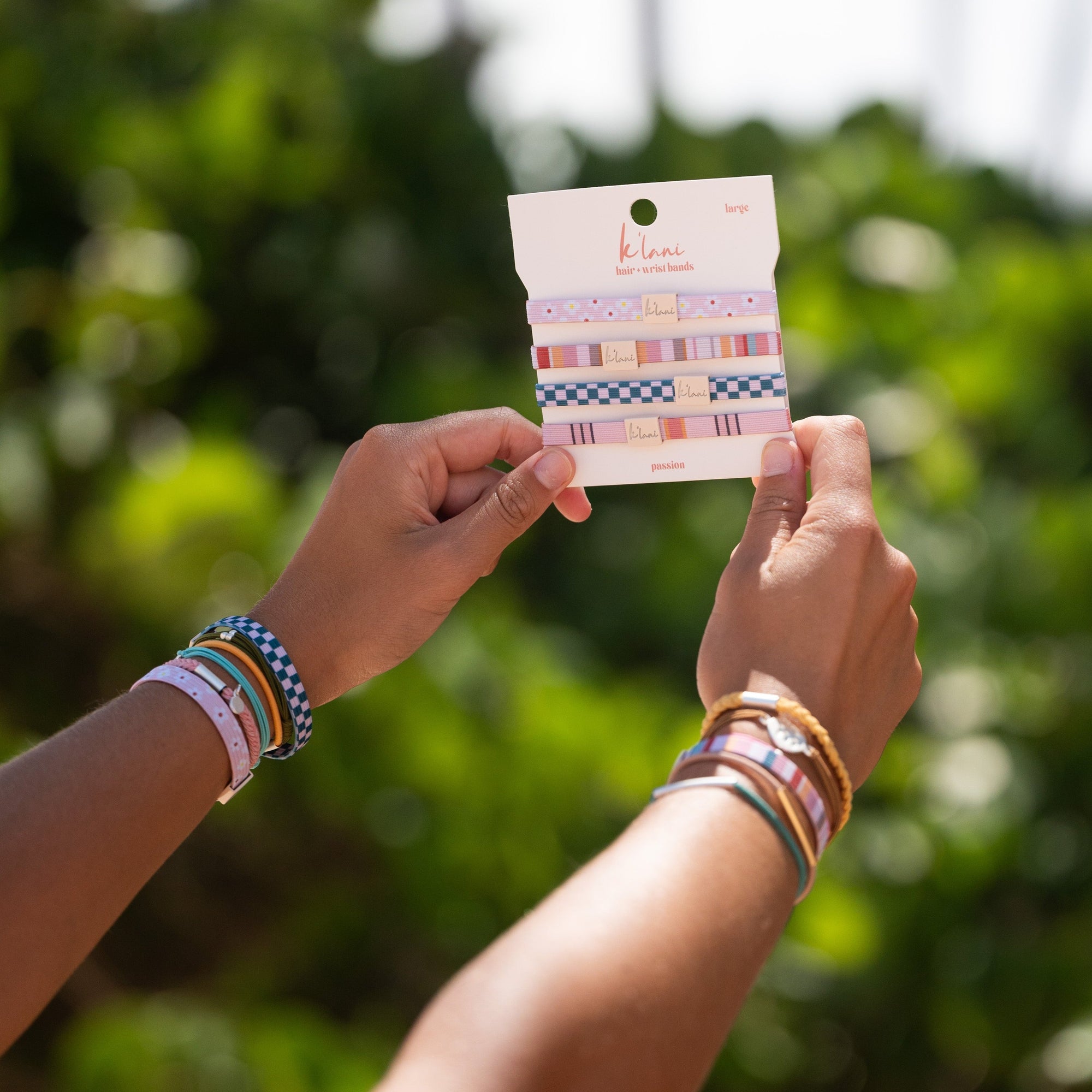 Hands holding a packaged set of patterned hair ties and wristbands with colorful designs