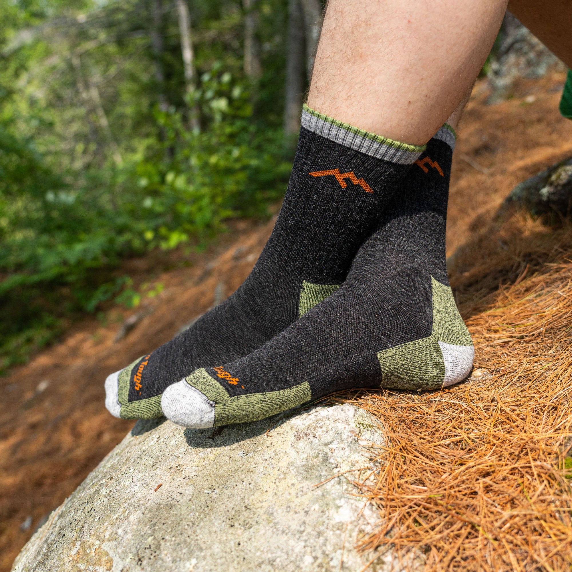 Charcoal quarter-crew hiking socks with olive green heel and toe accents, worn on rocky trail