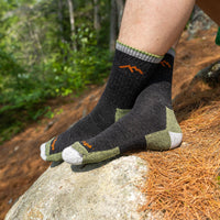 Charcoal quarter-crew hiking socks with olive green heel and toe accents, worn on rocky trail