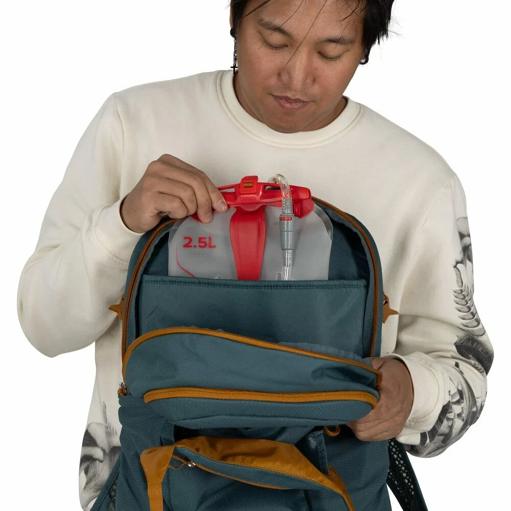 Person inserting a 2.5L hydration reservoir into a teal backpack's dedicated compartment