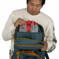 Person inserting a 2.5L hydration reservoir into a teal backpack's dedicated compartment