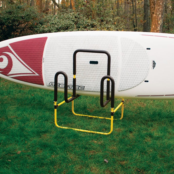 Yellow and black paddleboard cart stand holding white SUP board on grass