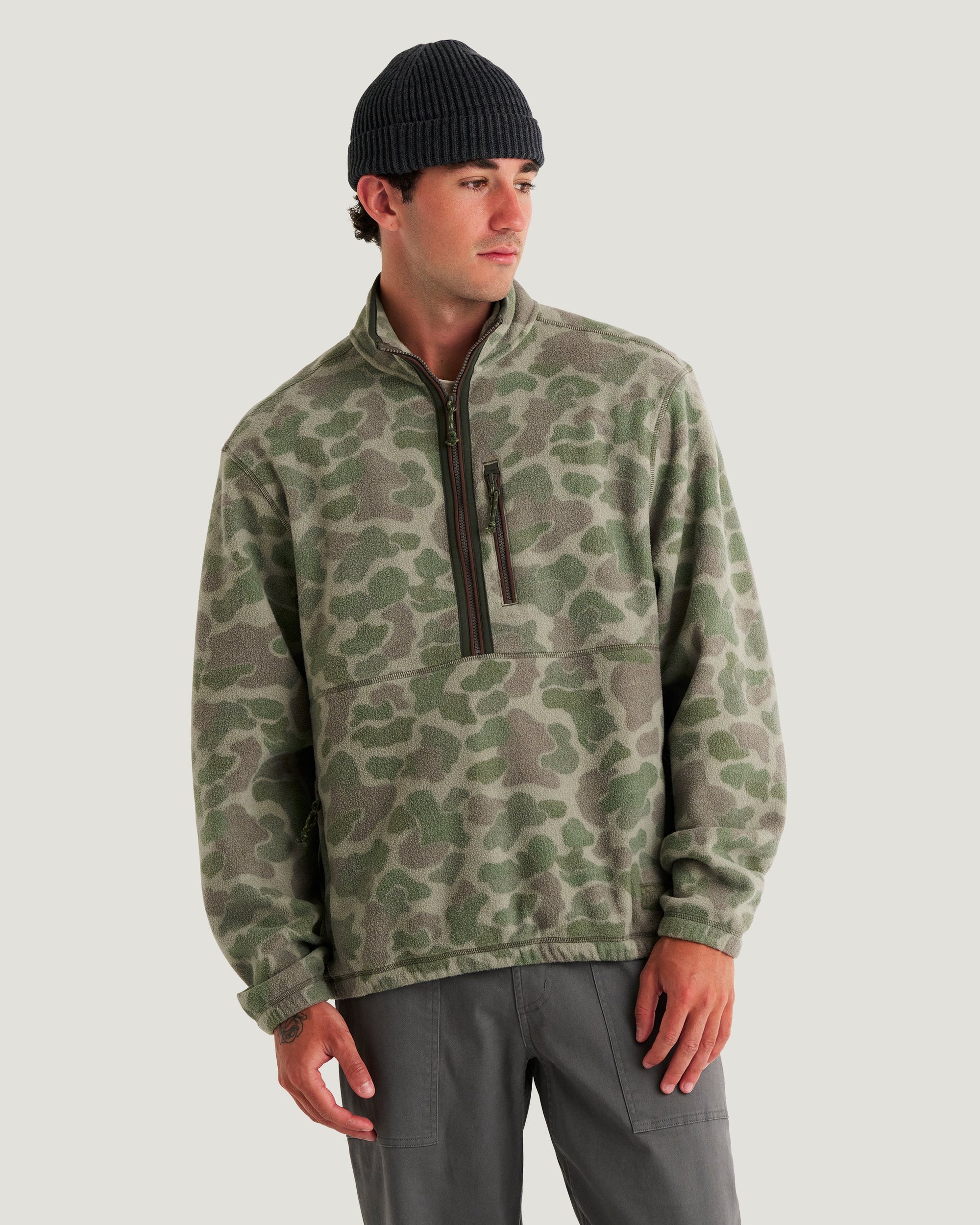 Men's camo fleece half-zip pullover with chest pocket, worn with dark beanie and gray pants