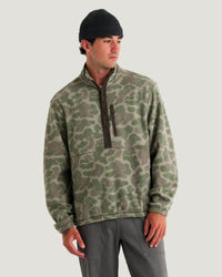 Men's camo fleece half-zip pullover with chest pocket, worn with dark beanie and gray pants