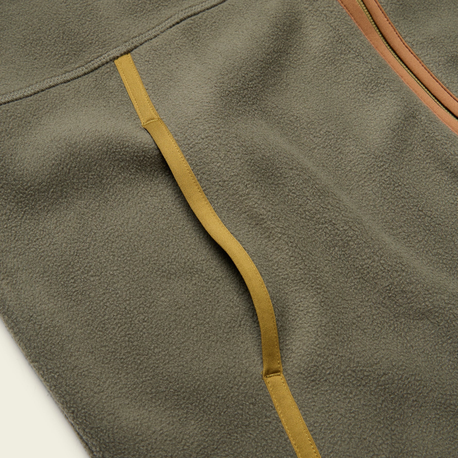 Close-up detail of fleece vest showing pocket opening with contrast woven strap and zipper trim