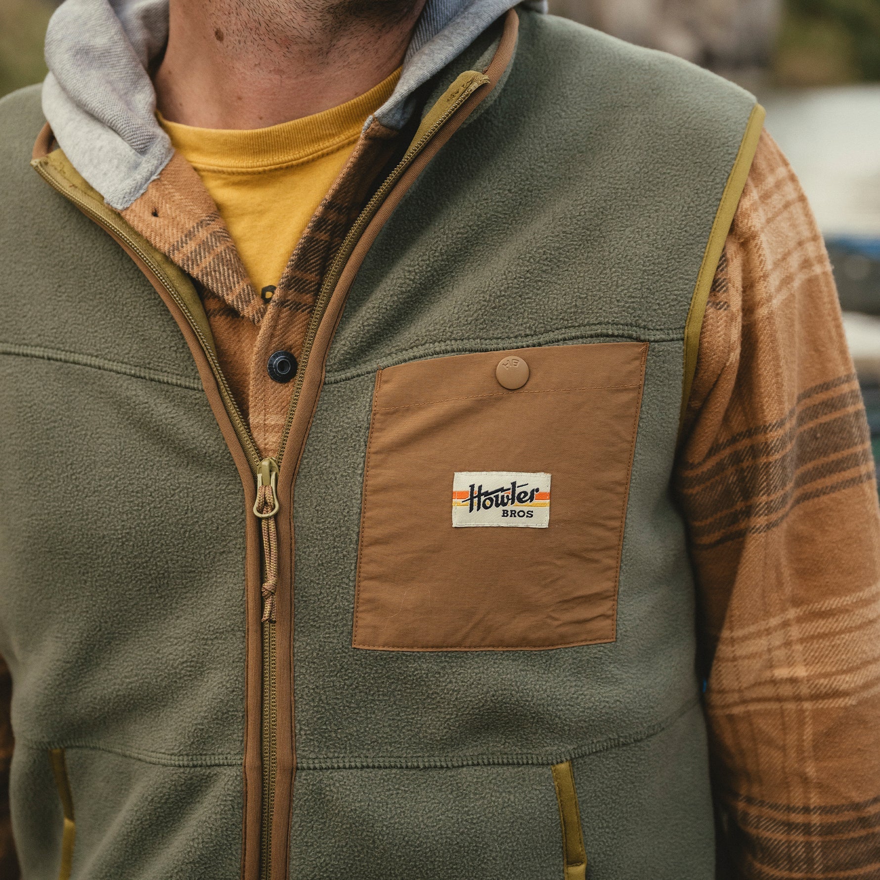 Men's fleece vest in olive green with zip front and tan chest pocket, lifestyle close-up