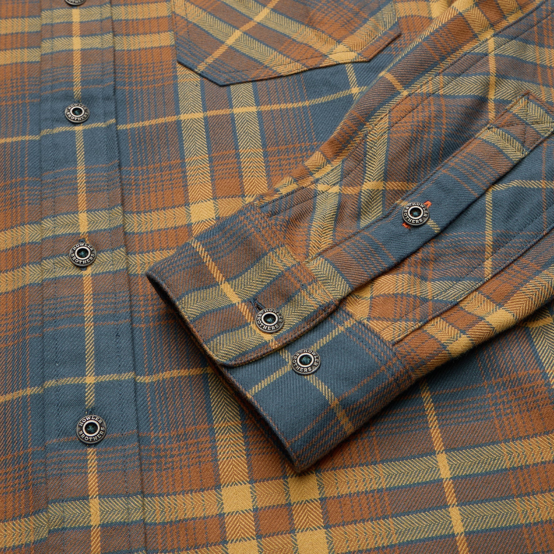Close-up detail of plaid flannel shirt cuff with branded snap buttons, showing herringbone weave