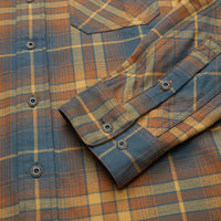 Close-up detail of plaid flannel shirt cuff with branded snap buttons, showing herringbone weave