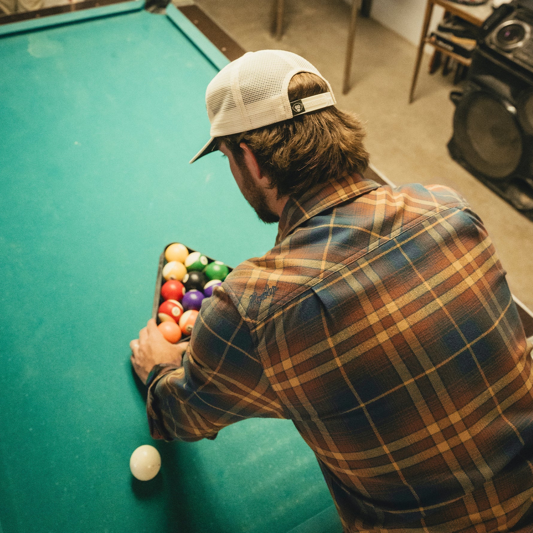 Man racking billiard balls wearing a plaid flannel shirt, viewed from behind