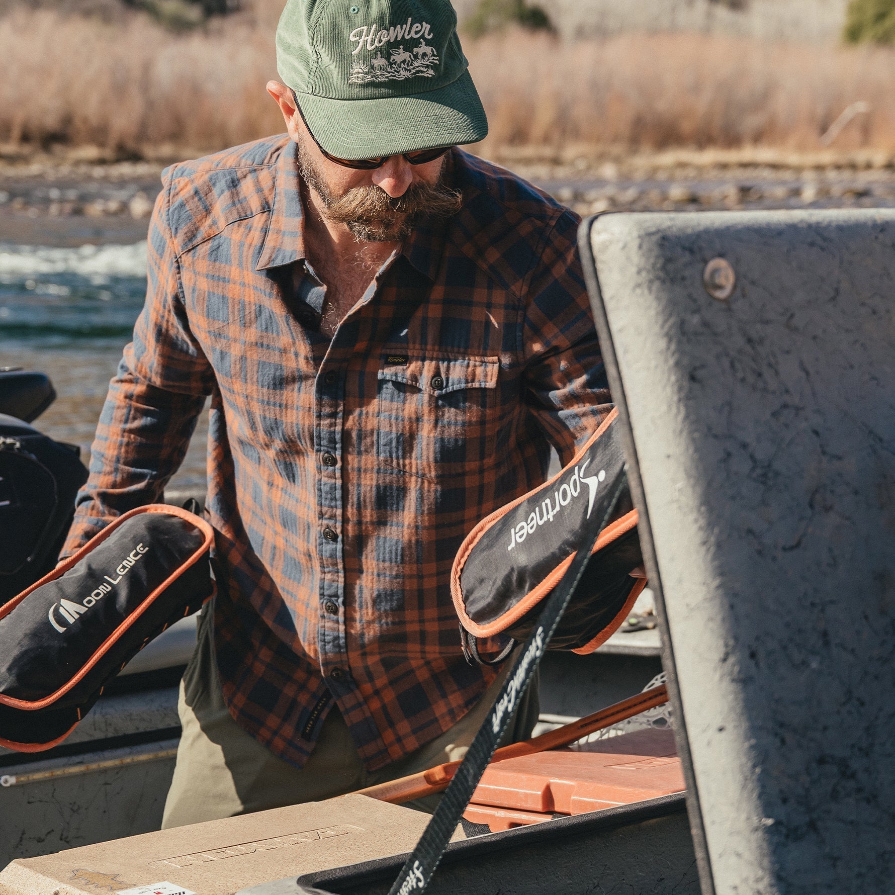 Man loading gear into a river boat wearing a plaid lightweight flannel shirt, lifestyle shot