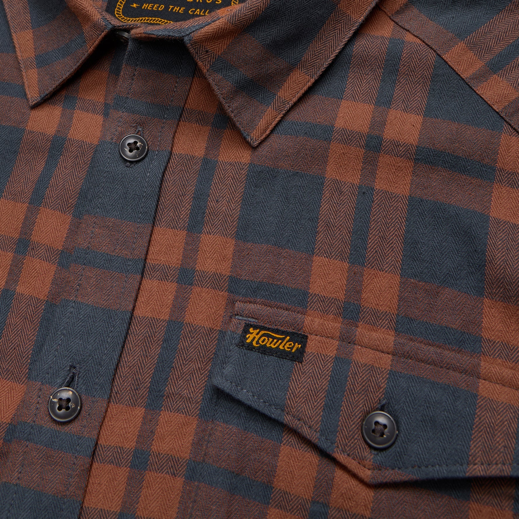 Close-up detail of plaid flannel shirt showing collar, buttons, chest pocket, and brand label