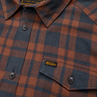 Close-up detail of plaid flannel shirt showing collar, buttons, chest pocket, and brand label
