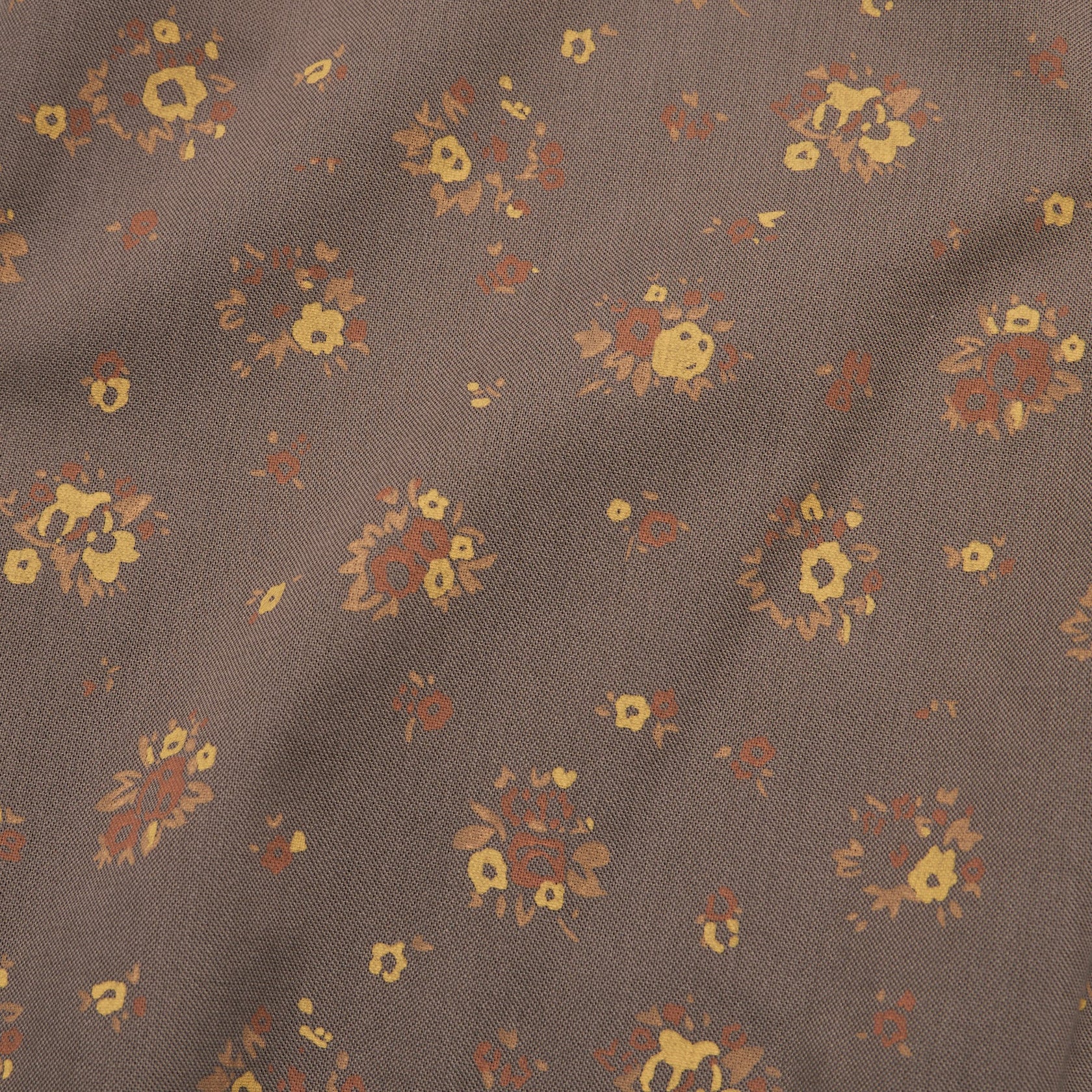 Close-up detail of floral print fabric with small bouquet clusters on taupe brown background