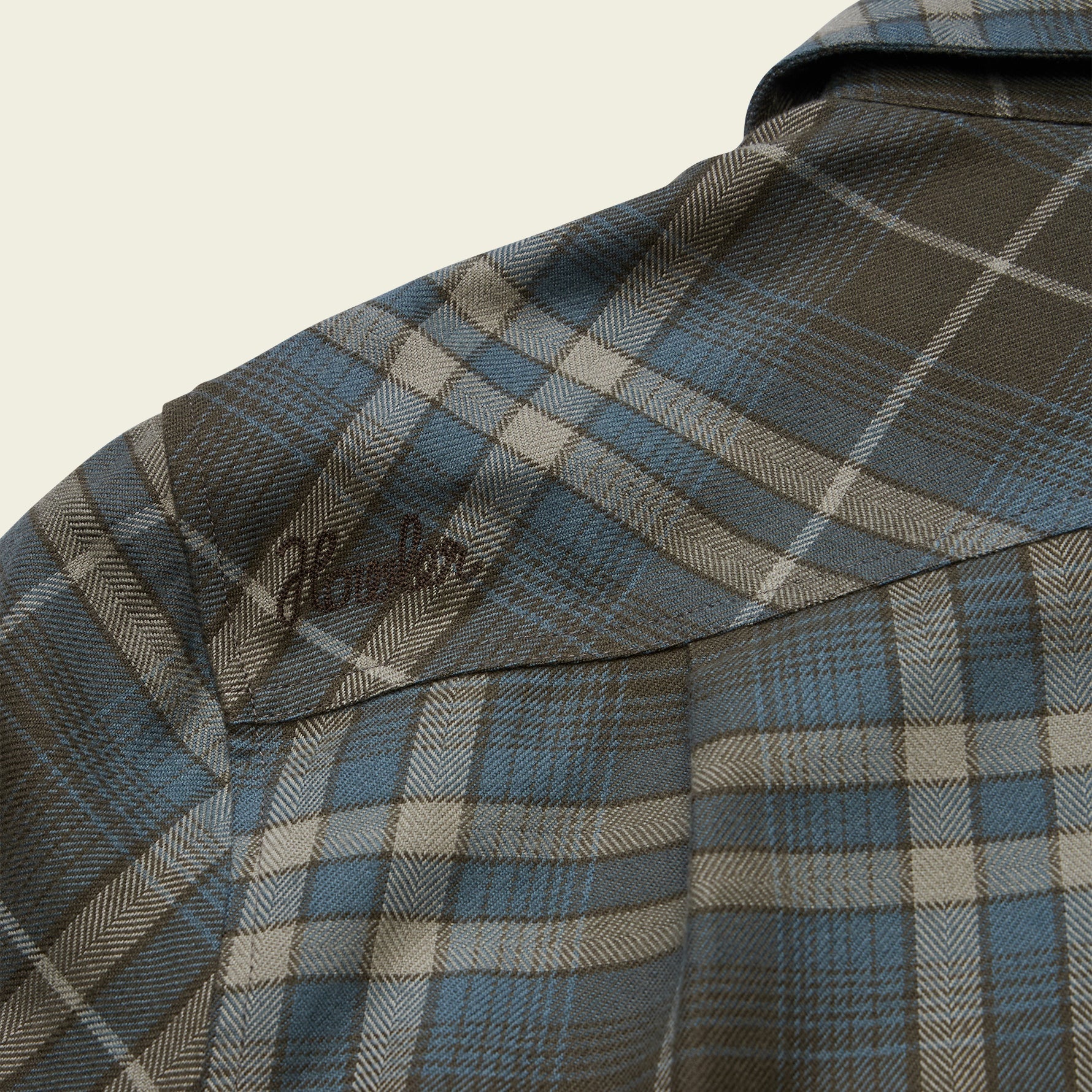 Close-up detail of plaid flannel shirt shoulder seam with embroidered script logo