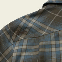 Close-up detail of plaid flannel shirt shoulder seam with embroidered script logo