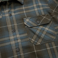 Close-up detail of plaid flannel shirt showing chest pocket, snap buttons, and herringbone weave texture