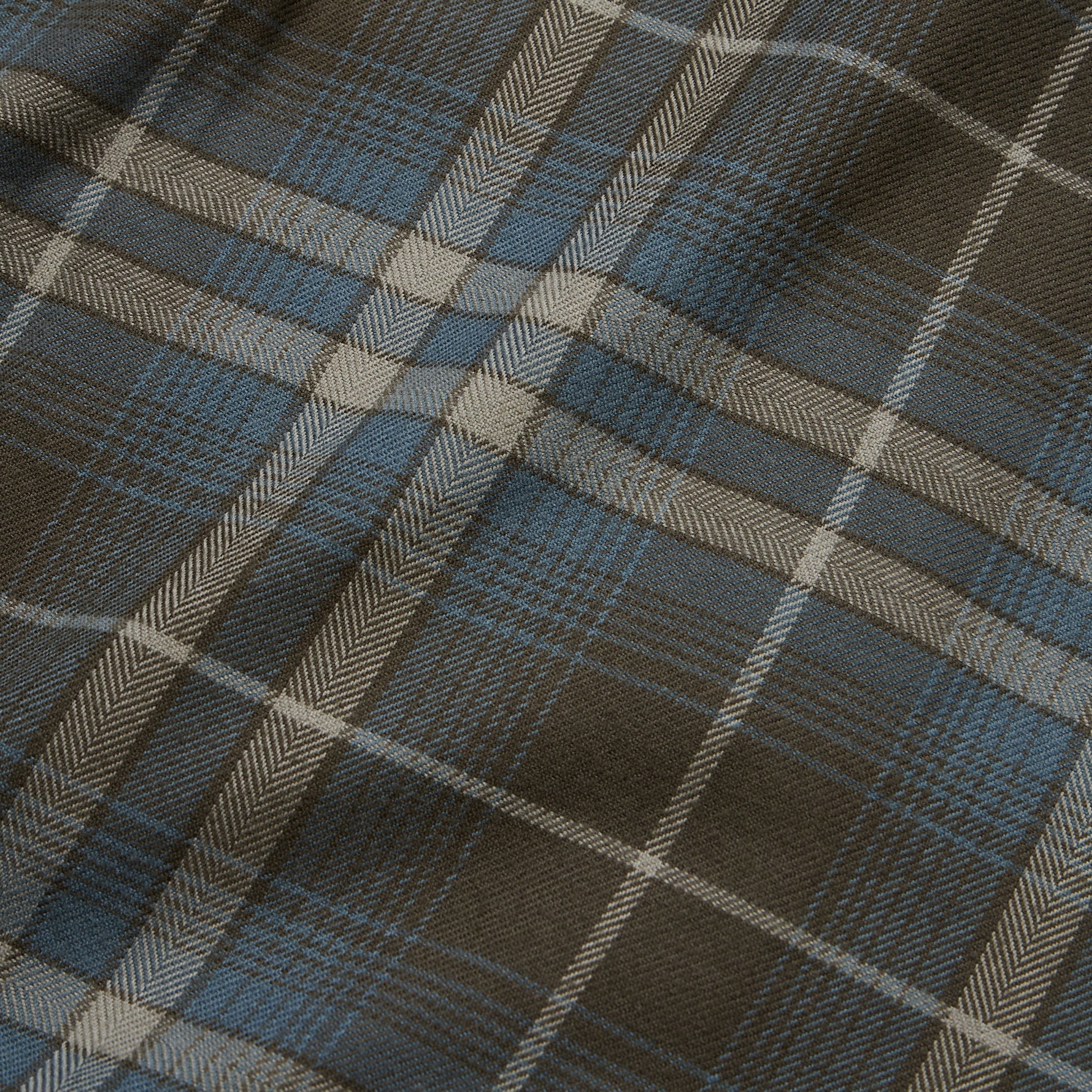 Close-up detail of plaid flannel fabric showing herringbone weave in brown, blue, and cream tones