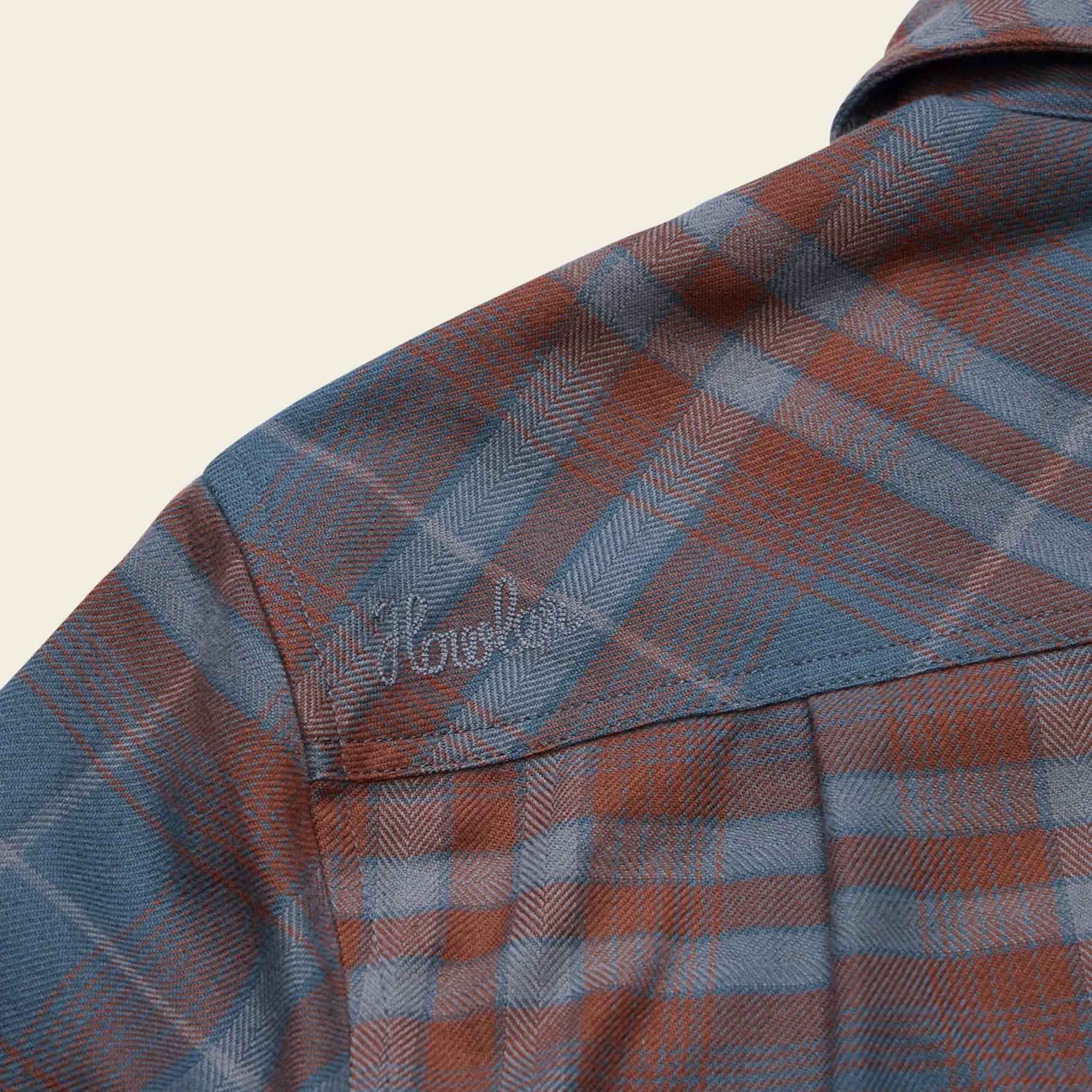 Close-up detail of plaid flannel shirt shoulder seam with embroidered script logo
