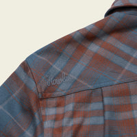 Close-up detail of plaid flannel shirt shoulder seam with embroidered script logo