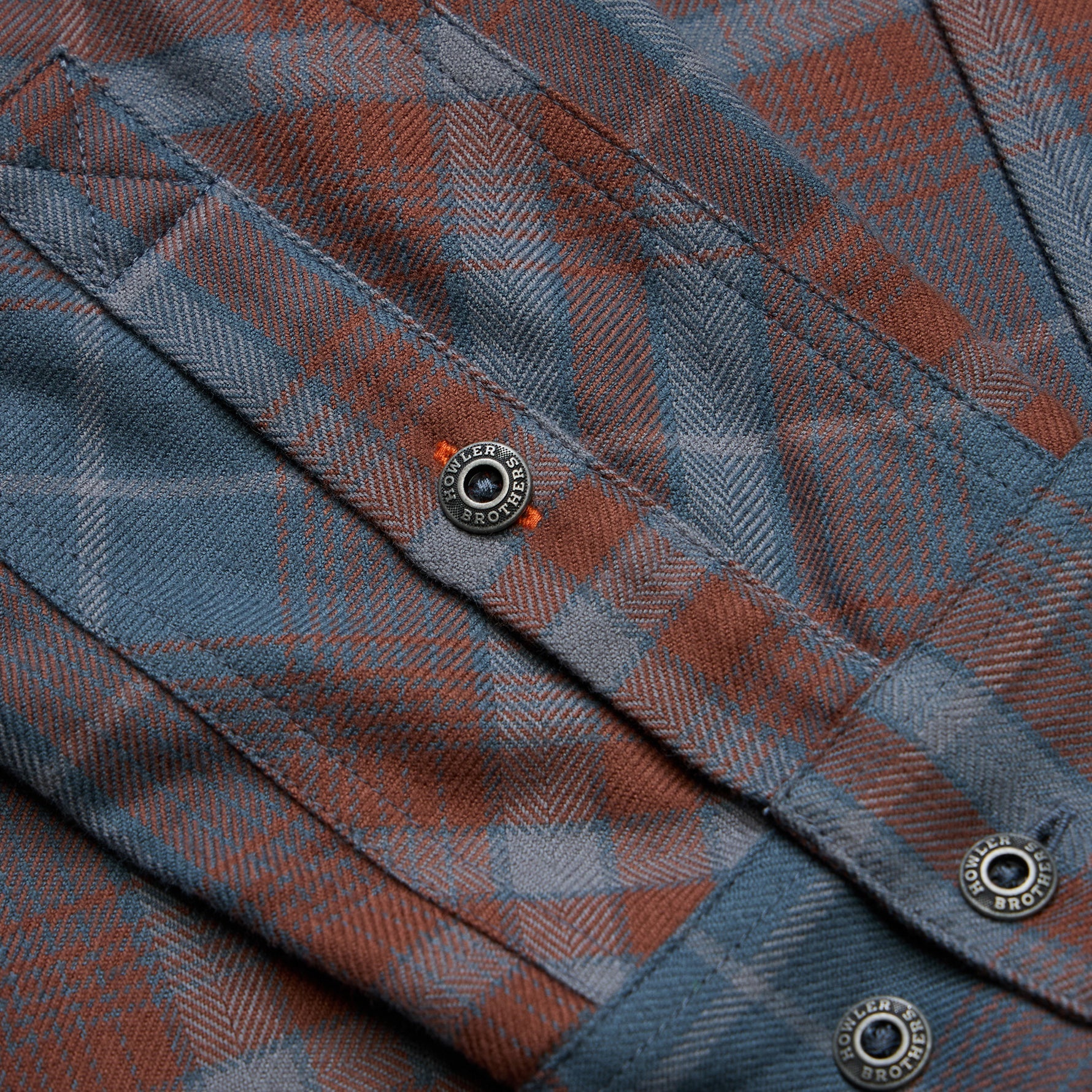 Close-up detail of plaid flannel shirt pocket with branded metal snap buttons