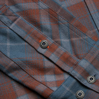 Close-up detail of plaid flannel shirt pocket with branded metal snap buttons