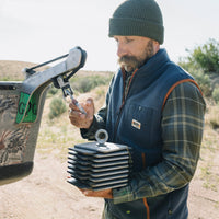 Man wearing a dark navy fleece vest over plaid shirt in outdoor desert setting