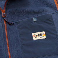 Close-up detail of navy fleece vest chest pocket with snap button and brand patch