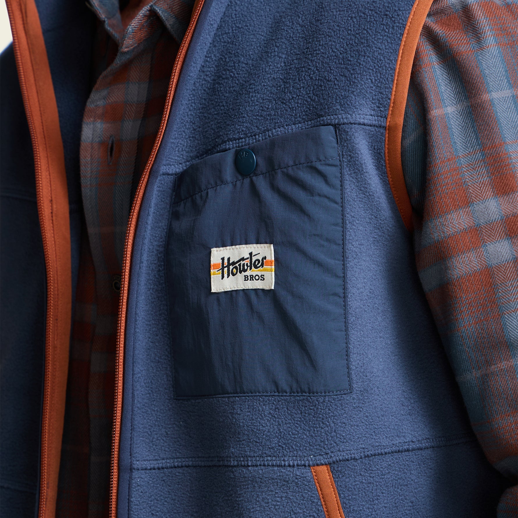 Close-up detail of men's fleece vest chest pocket with brand patch label and snap closure