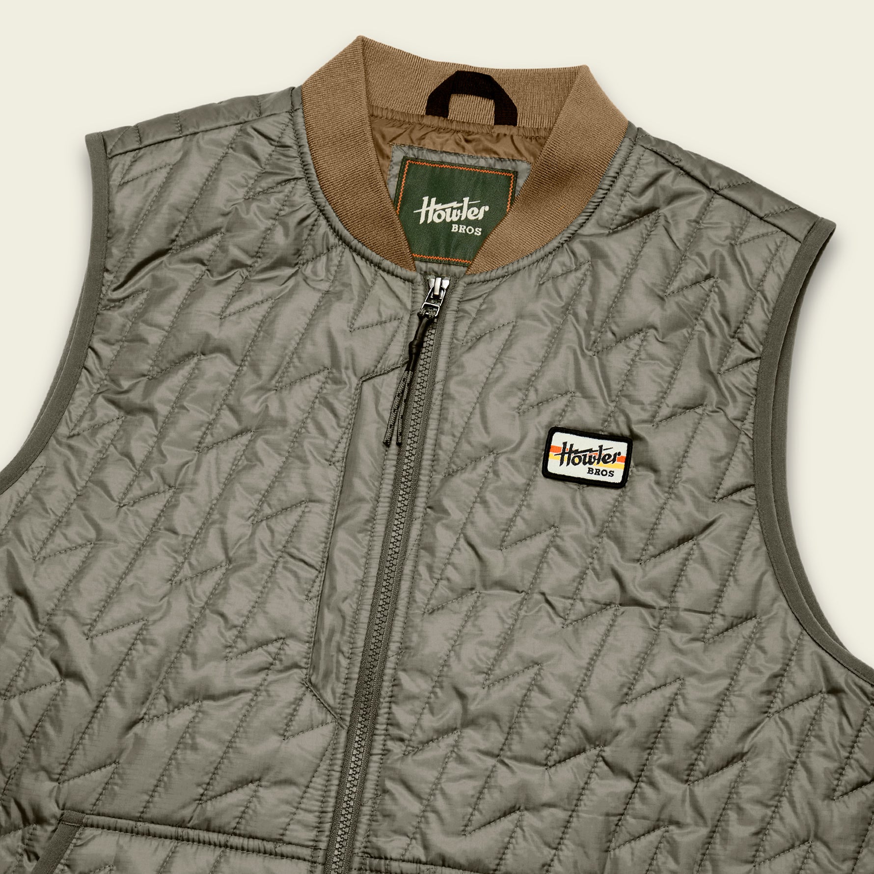 Quilted sleeveless vest with diagonal stitch pattern, zip front, ribbed collar, and logo patch