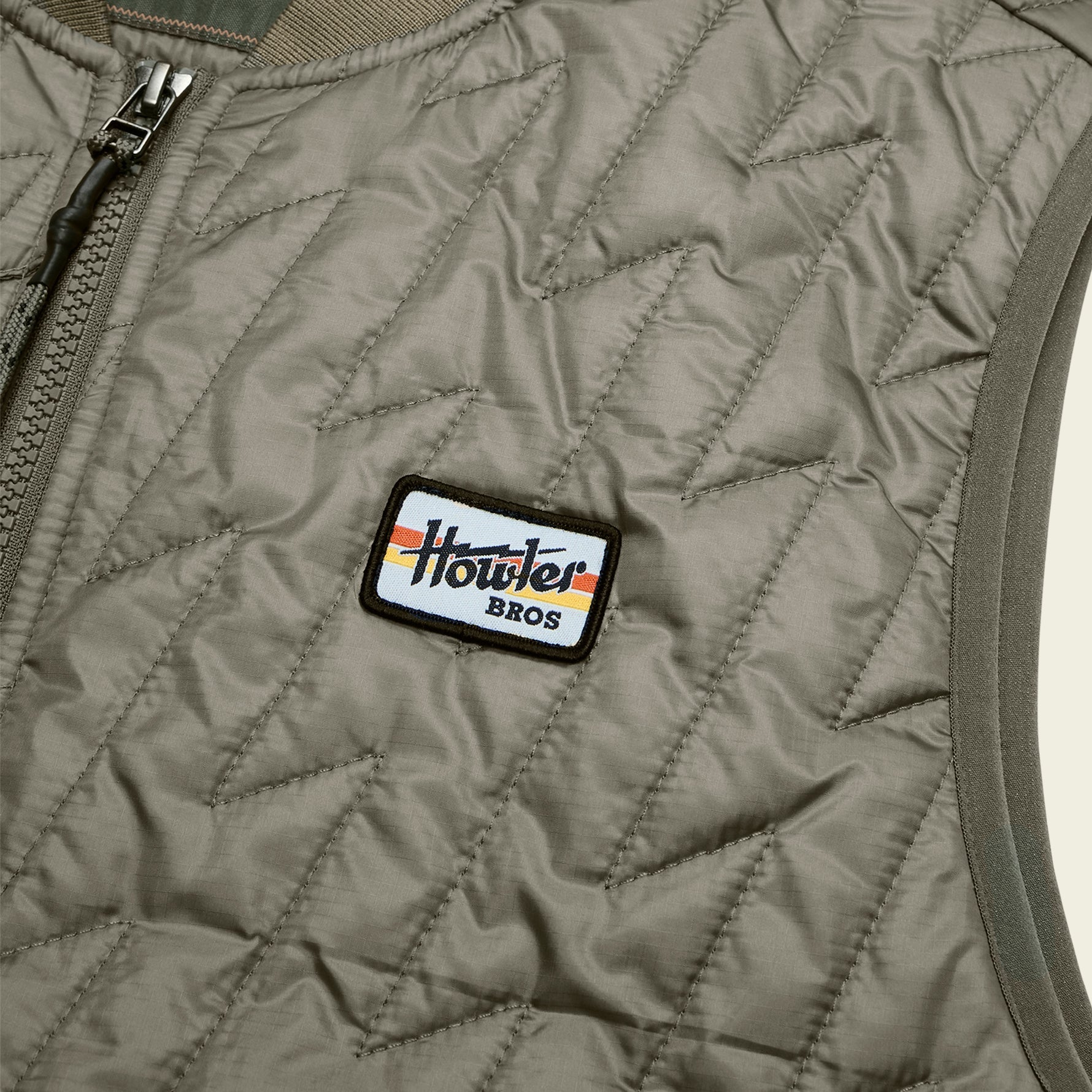 Close-up detail of quilted vest chest area showing brand patch and zipper