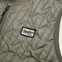 Close-up detail of quilted vest chest area showing brand patch and zipper
