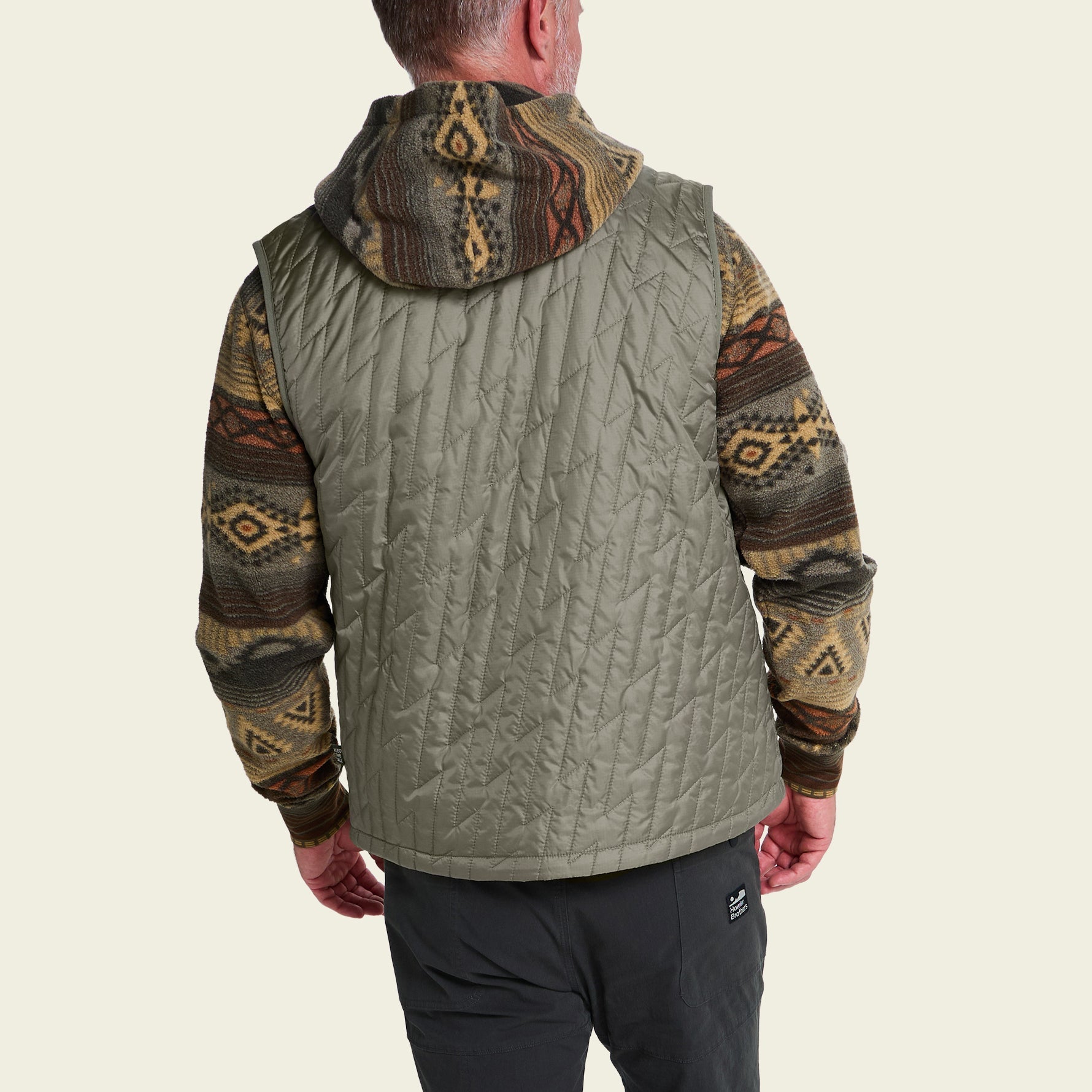 Back view of quilted sleeveless vest with hood, worn over patterned long-sleeve shirt