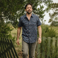 Men's short-sleeve snap-button shirt in dark navy floral print, worn on model outdoors