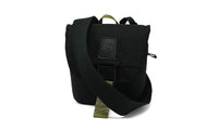 Small black canvas crossbody pouch with olive green strap, buckle closure, and logo patch, front view