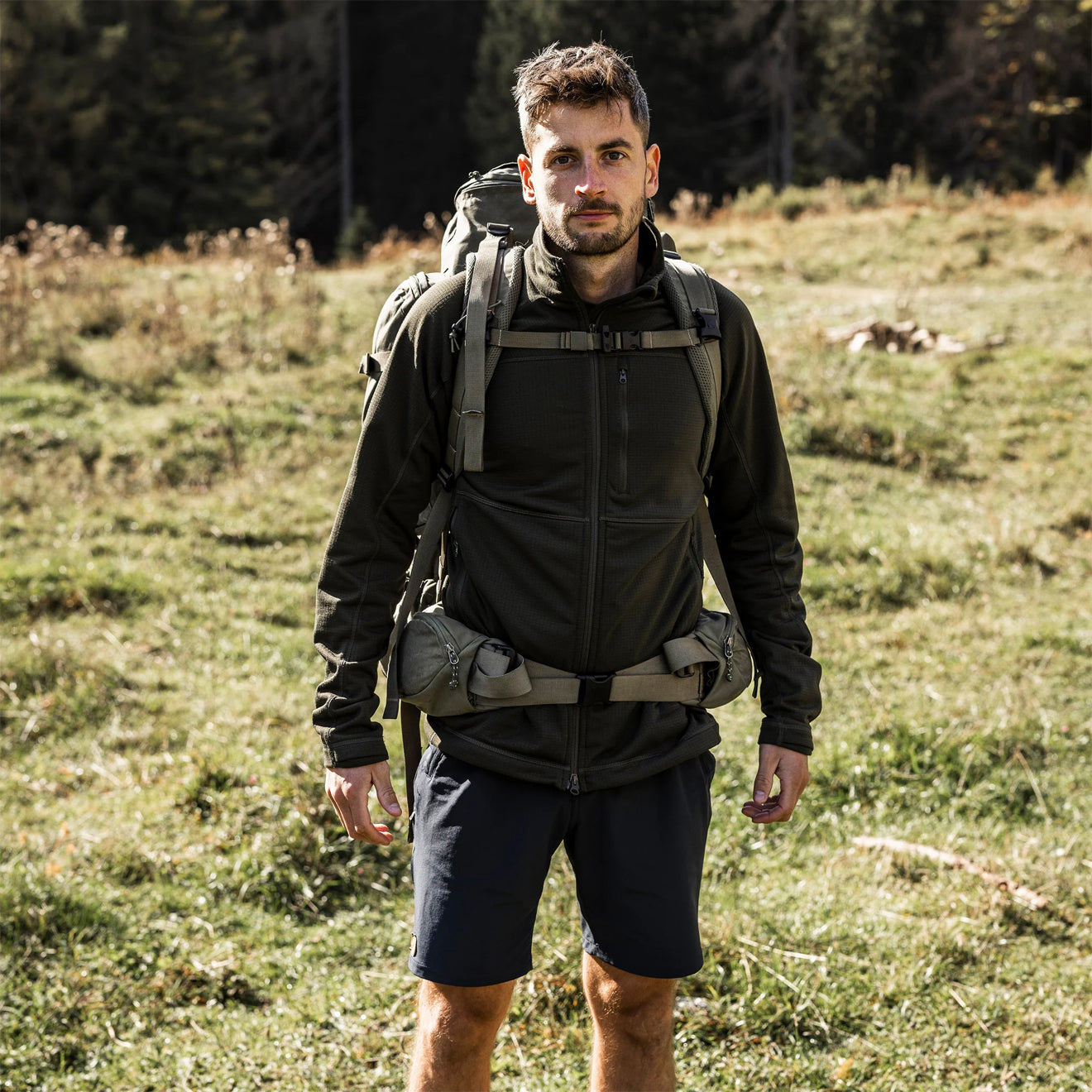 Man wearing dark outdoor shorts with hiking backpack in natural field setting